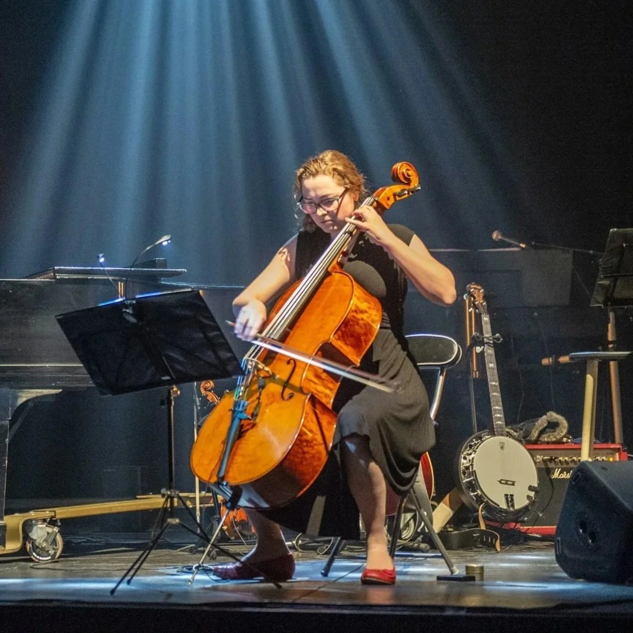 Violoncelista a tocar em palco, iluminada por um foco
